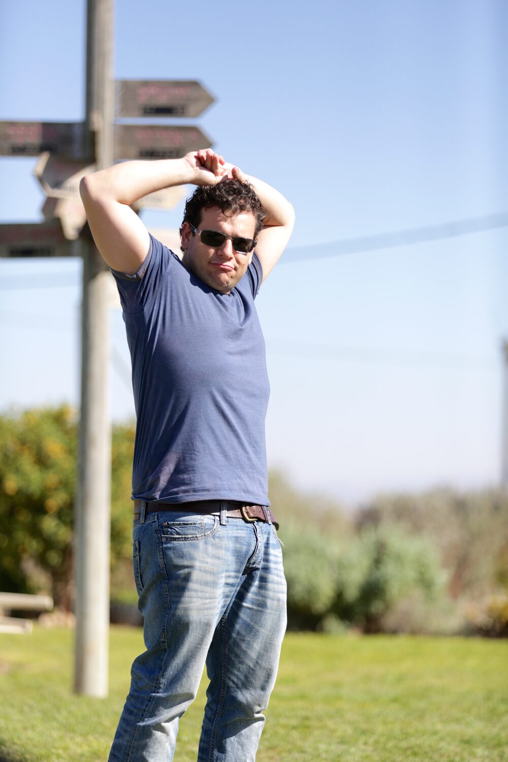Pablo Srabstein standing at a cluster of directional signposts, sunglasses, arms overhead